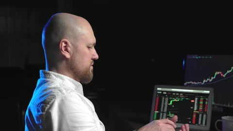 Side view of a man sitting at a computer and looking at an online stock market Stock Footage 180359023
