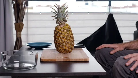 Side view of man sitting on the sofa cutting a pineapple at home. Stock Footage 126645891