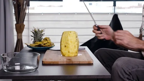 Side view of man sitting on the sofa cutting a pineapple at home. Stock Footage 126645902