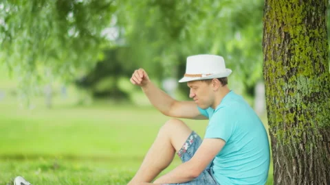 Side view of a man sitting under a tree in the park Stock Footage 148236428