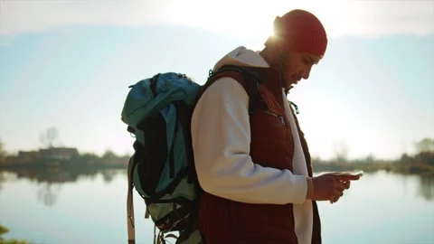 Side view of man with tourist backpack on background of lake using smartphone Stock Footage 268467320