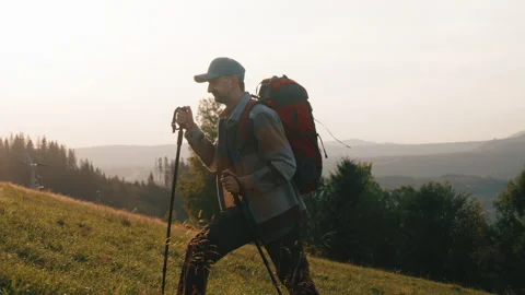 Side view man with trekking poles walking on meadow hill overlooking mountains Stock Footage 290171701