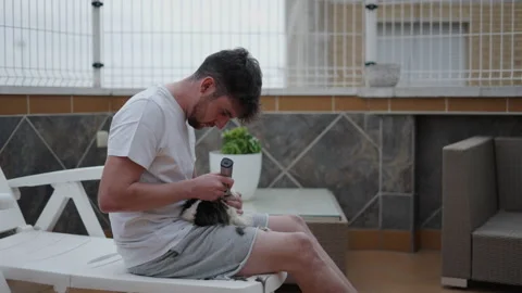 Side view of man trimming its guinea pig hair sitting at balcony outdoors Stock Footage 221234389