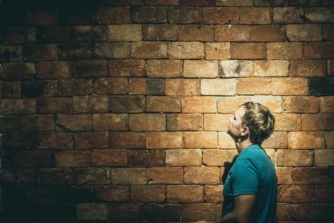 Side view man under life crisis problems stand facing looking on brown brick Foto stock