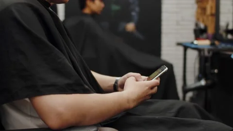 Side view of a man using smartphone in barbershop. Hipster guy sitting in chair Stock Footage 221411200