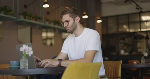 Side view of man who sits in cafe in daytime and using the laptop for the remote Video stock 164491608