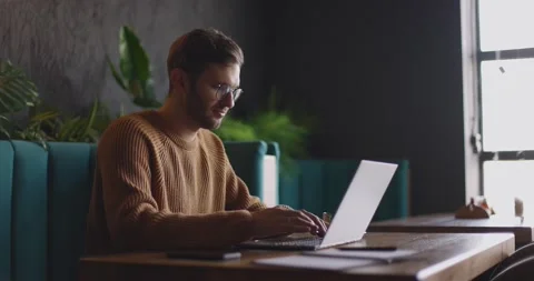 Side view of man who sits in cafe in daytime and using the laptop for the remote Stock Footage 164492292