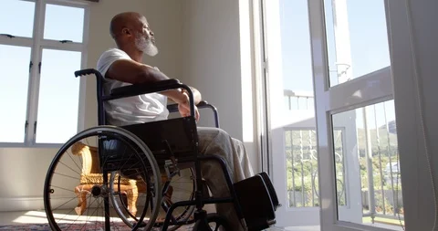 Side view of mature black handicap man sitting on wheelchair near the window at Stock Footage