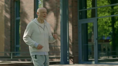Side view of mature man runner running through the street and listen to music Stock Footage 223734011