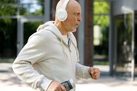 Side View of the Mature Man Runner Is Jogging In The Street Wearing Headphones Stock Photos
