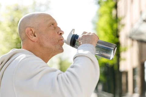 Side View of the Mature Positive Runner Drinking Water from the Sport Bottle Stock Photos