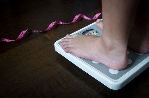Side view of measuring tape and feet on weight scale . Weight loss concept. Stock Photos