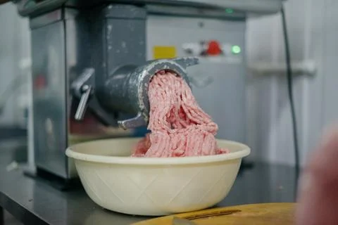 Side view of a meat grinder and minced meat falling into a bowl. Stock Photos