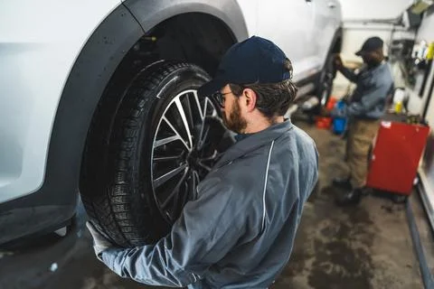 Side view of a mechanic changing a car wheel, his colleague in the background Stock Photos