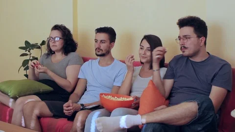 A side view of mid shot of four friends watching TV while chating  Stock Footage 93873288
