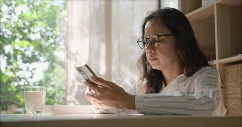 Side view. Middle Aged Asian Woman with Glasses Using Smartphone in Living Room 库存影片 338168698