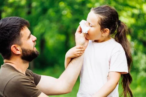 Side view of middle-aged bearded handsome man father wiping daughters nose with Stock Photos