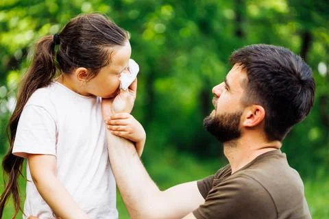 Side view of middle-aged bearded careful man father wiping daughters nose with Stock Photos