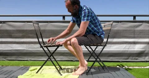 Side view of a middle-aged man sanding a chair on the terrace of his house on Stock Footage 154636576