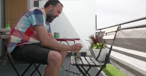 Side view of a middle-aged man dressed in summer clothes varnishing some chai Stock Footage 154636672