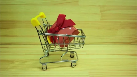 Side view of mini shopping trolley with red gift box moving back and forth Video stock 326243300