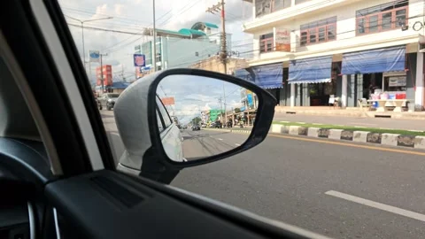 Side view mirror of a car capturing a bustling urban street with moving traffic Stock Footage 340813332