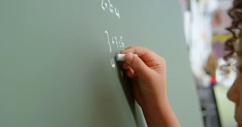 Side view of mixed-race schoolgirl solving math problem on chalkboard in Stock Footage 106946293