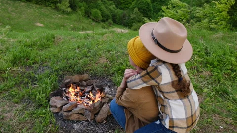 Side view of mom and cute little daughter child in hat sit near campfire Stock Footage 195865733