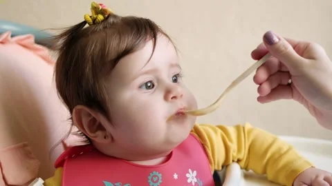 Side view mother feeding her baby daughter 9 month infant girl eating with sp Stock Footage 144666275