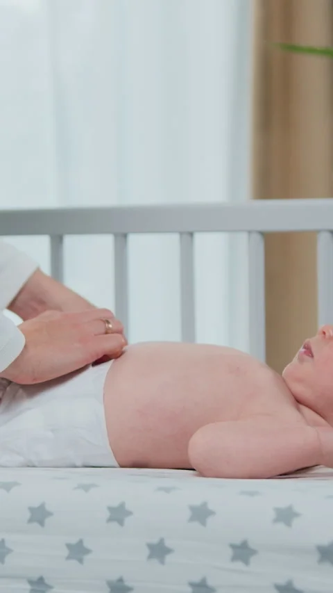 Side view. Mother puts on clean diaper dressing newborn boy lying on bed at home Stock Footage 334680629