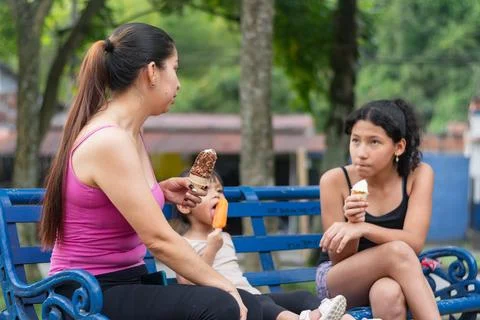 Side view of a mother talking with her daughters as they eat ice cream on a.. Stock Photos
