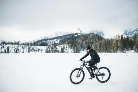 Side view of mountain biker riding in snow outdoors in winter nature. Stock Photos