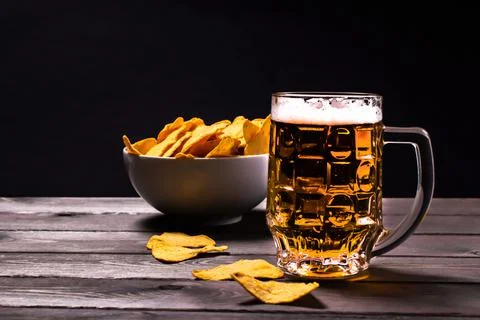 Side view of a mug of cold frothy beer with nachos corn chips on a wooden bac Stock Photos