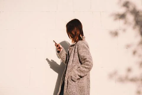 Side view of non-binary woman using smart phone standing against wall Stock Photos