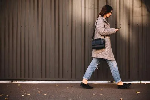 Side view of non-binary woman using smart phone walking against wall Stock Photos