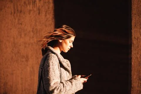Side view of non-binary woman using smart phone walking against wall Stock Photos