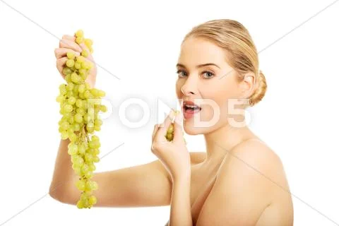 Side view of nude woman eating grapes, looking at the camera Stock