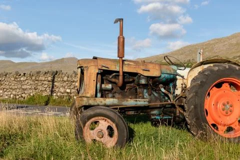 Side view of an old abandoned rusty agricultural tractor in a grass field Stock Photos
