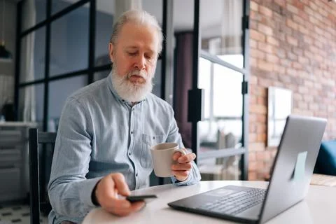 Side view of older 60s bearded male working on laptop computer and using Stock Photos