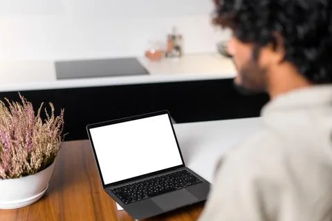 Side view at optimistic Indian man wearing hoodie sitting at desk and using Stock Photos