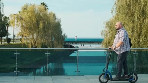 Side view of overweight man riding e-scooter in the city on the btidge. Plus Stock Footage 270586778
