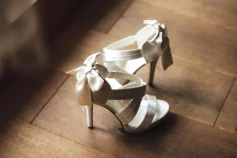Side view of pair of white wedding shoes standing on wooden floor. Shoes are Stock Photos
