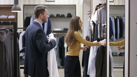 A side view panoramic shot of a young clothing shop consultant helping a male Stock Footage 132529720