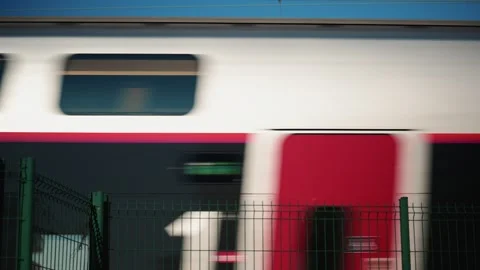 Side view of a passenger train moving past a green fence near the railway tracks Stock Footage 325808206