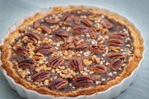 Side view of pecan pie and nuts in ceramic bowl, handmade, on striped pattern Fotos de archivo