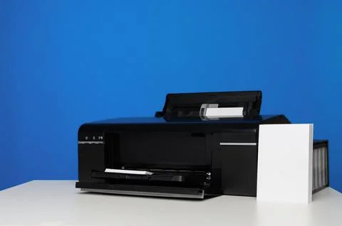 Side view of photo printer and blank sheets of photo paper on blue background Stock Photos