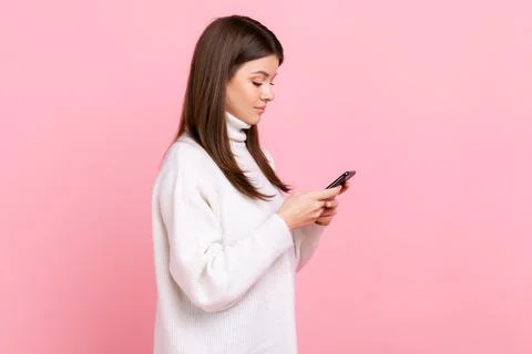 Side view portrait of female using smartphone, checking social networks, has Stock Photos