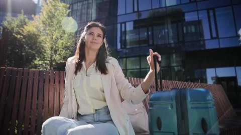 Side view portrait of gorgeous young woman sitting on bench with luggage aside Stock Footage 262143564