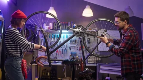 Side-view portrait of handsome young caucasian man repairing bicycle with cute Stock Footage 232866700