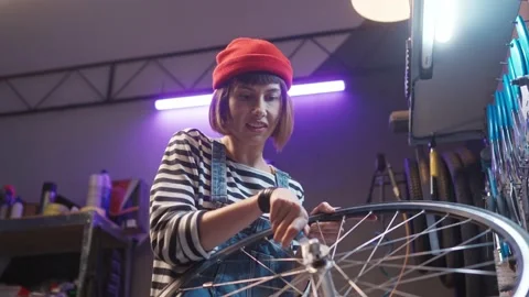 Side-view portrait of happy young caucasian female worker fixing bike wheel at Stock Footage 232867729